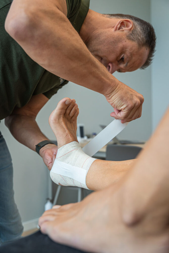 Enkelverzwikking wordt getapet door fysio op de behandeltafel
